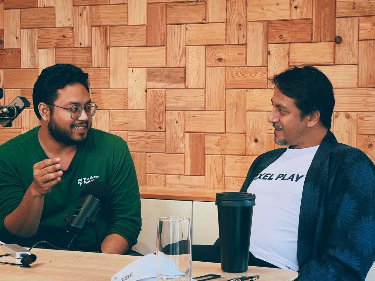 Harith merakam The Green Factor Podcast bersama tetamu di hadapan dinding kayu pain guna semula.