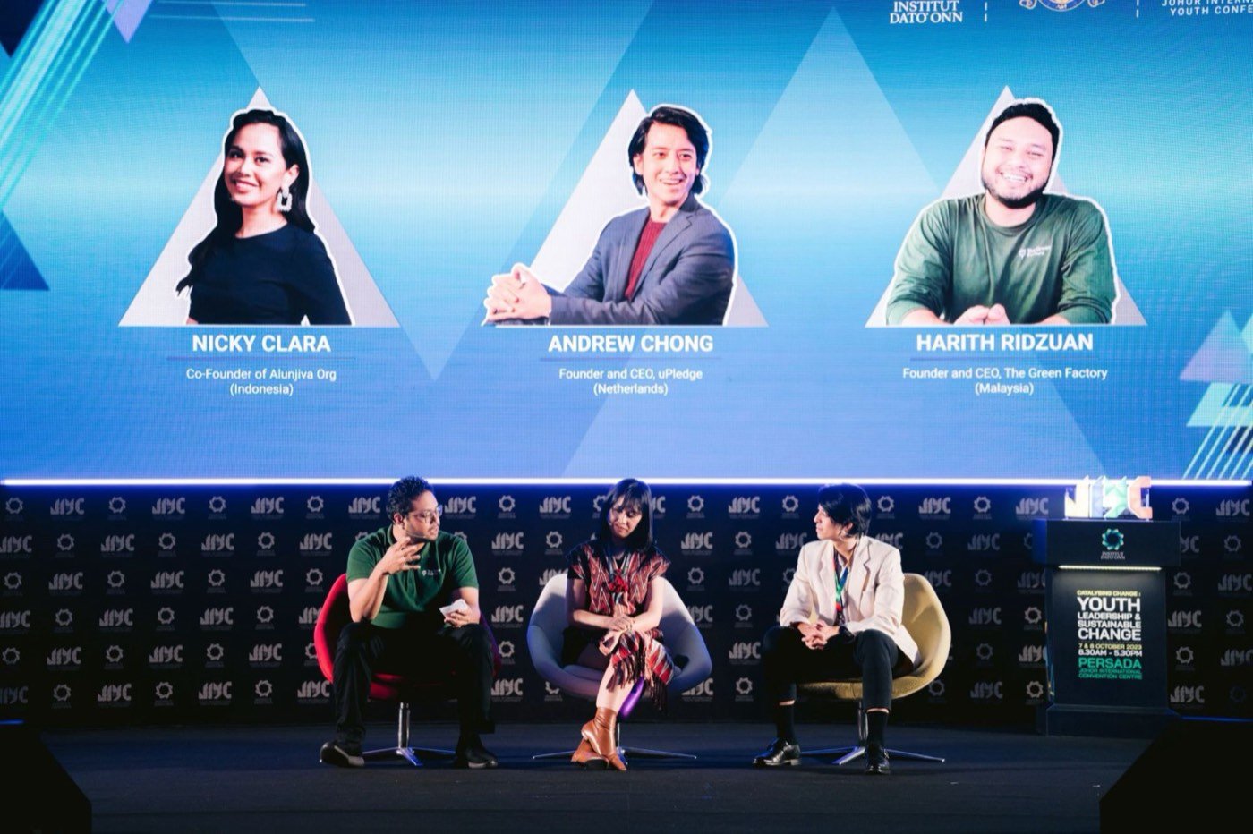 Harith bercakap dalam sesi panel Johor International Youth Conference dengan senarai penceramah pada skrin.